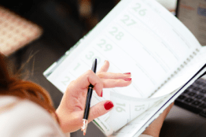 Scheduling a Home Sale Consultation – Ivy Home Solutions DFW Close-up of a woman holding a pen and flipping through a calendar planner, preparing to schedule a home sale consultation in Dallas-Fort Worth.