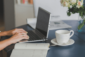 Working With Ivy Home Solutions – Coffee, Planning & Offers in DFW Hands typing on a laptop next to a planner and coffee cup – representing Ivy Home Solutions writing a cash offer for a Dallas homeowner.